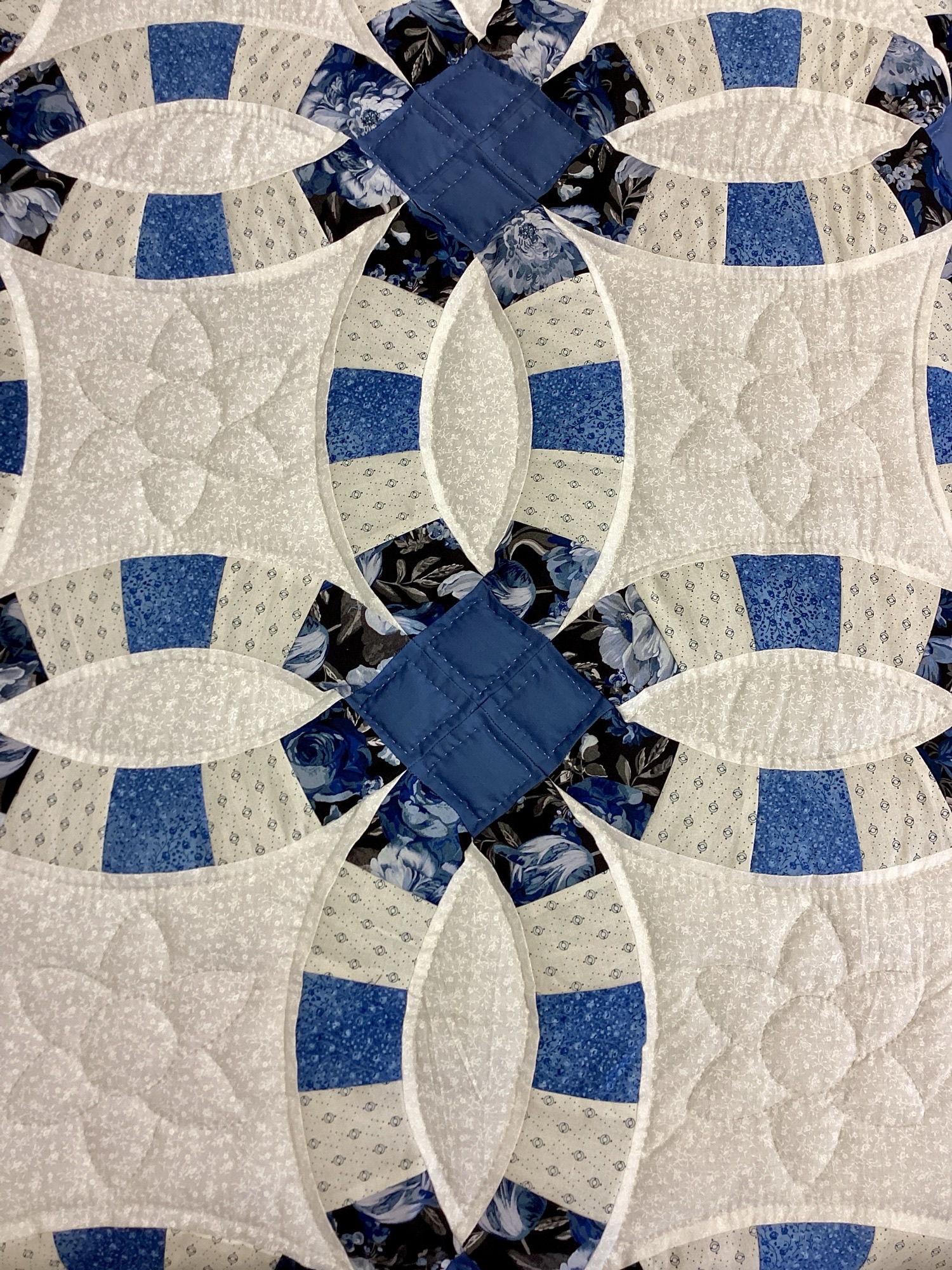 Close up of Hand-stitched blue Double Wedding Ring quilt with floral fabrics and white background