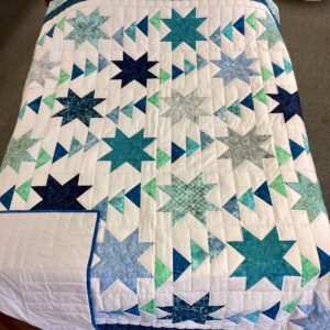 Handmade Lancaster County Flight of Geese quilt with blue and aqua star blocks, Flying Geese pattern, white background and navy border