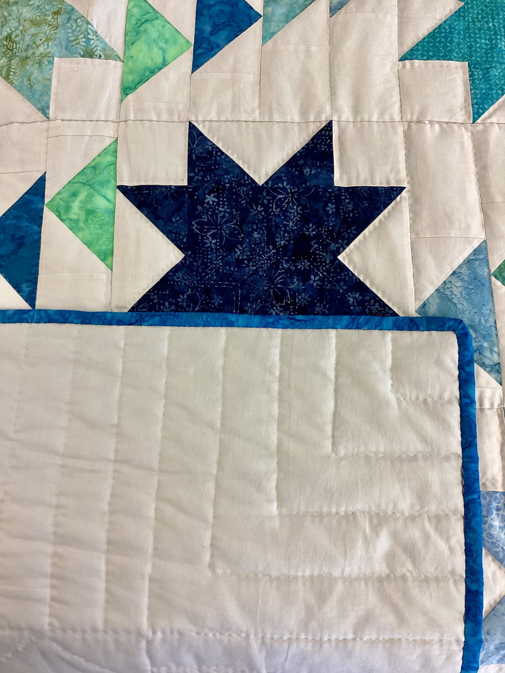 Backing of Handmade Lancaster County Flight of Geese quilt with blue and aqua star blocks, Flying Geese pattern, white background and navy border