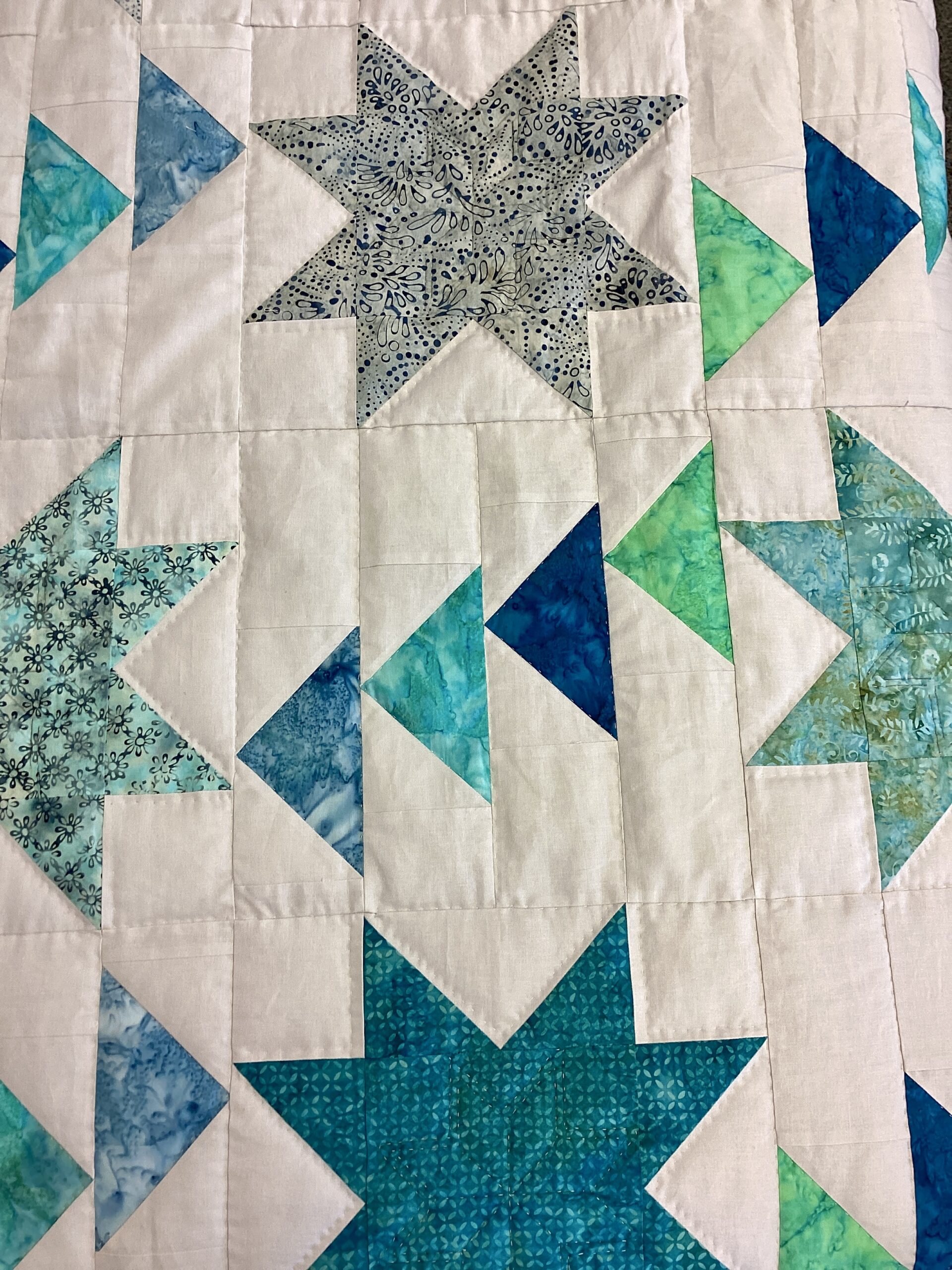 Close up of Handmade Lancaster County Flight of Geese quilt with blue and aqua star blocks, Flying Geese pattern, white background and navy border