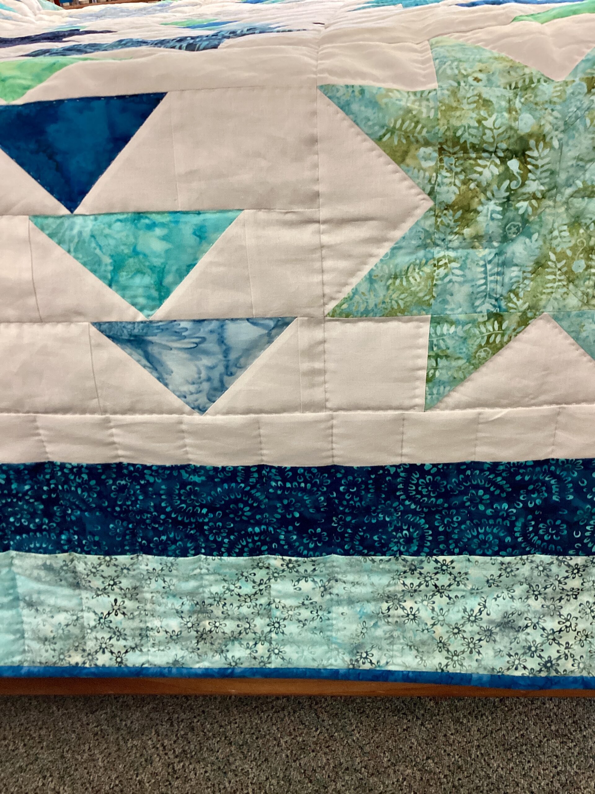 Close up of Handmade Lancaster County Flight of Geese quilt with blue and aqua star blocks, Flying Geese pattern, white background and navy border
