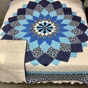 Handmade Lancaster County Amish Giant Dahlia quilt with navy blue and sky blue floral petals on a white background displayed on a king bed