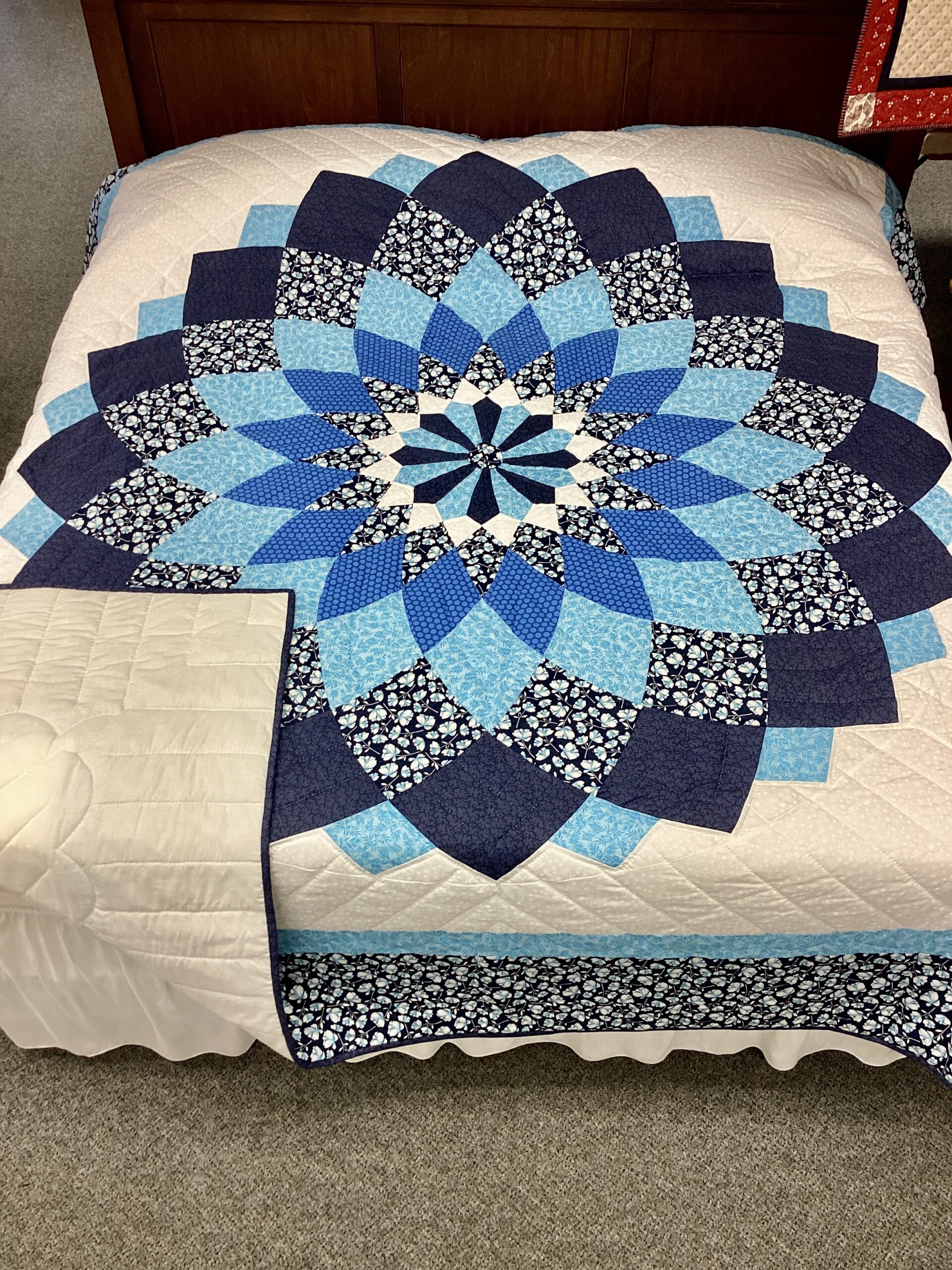 Handmade Lancaster County Amish Giant Dahlia quilt with navy blue and sky blue floral petals on a white background displayed on a king bed