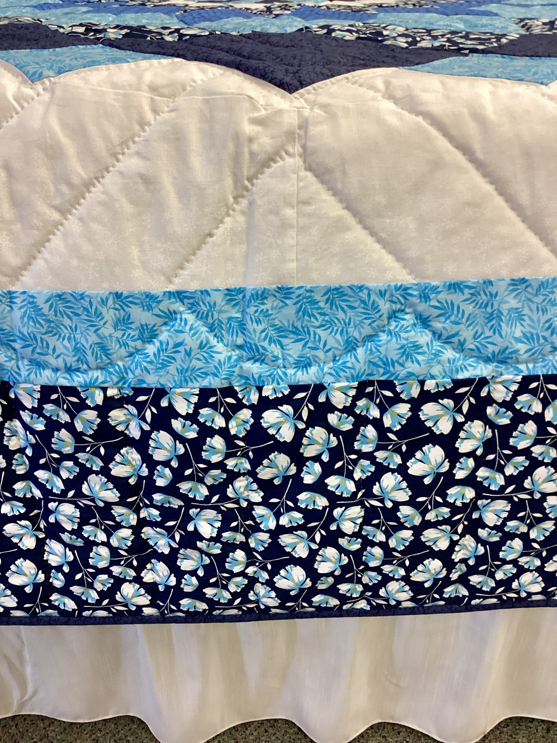 Close-up of blue floral border on handmade Giant Dahlia Amish quilt with cream background and decorative quilting