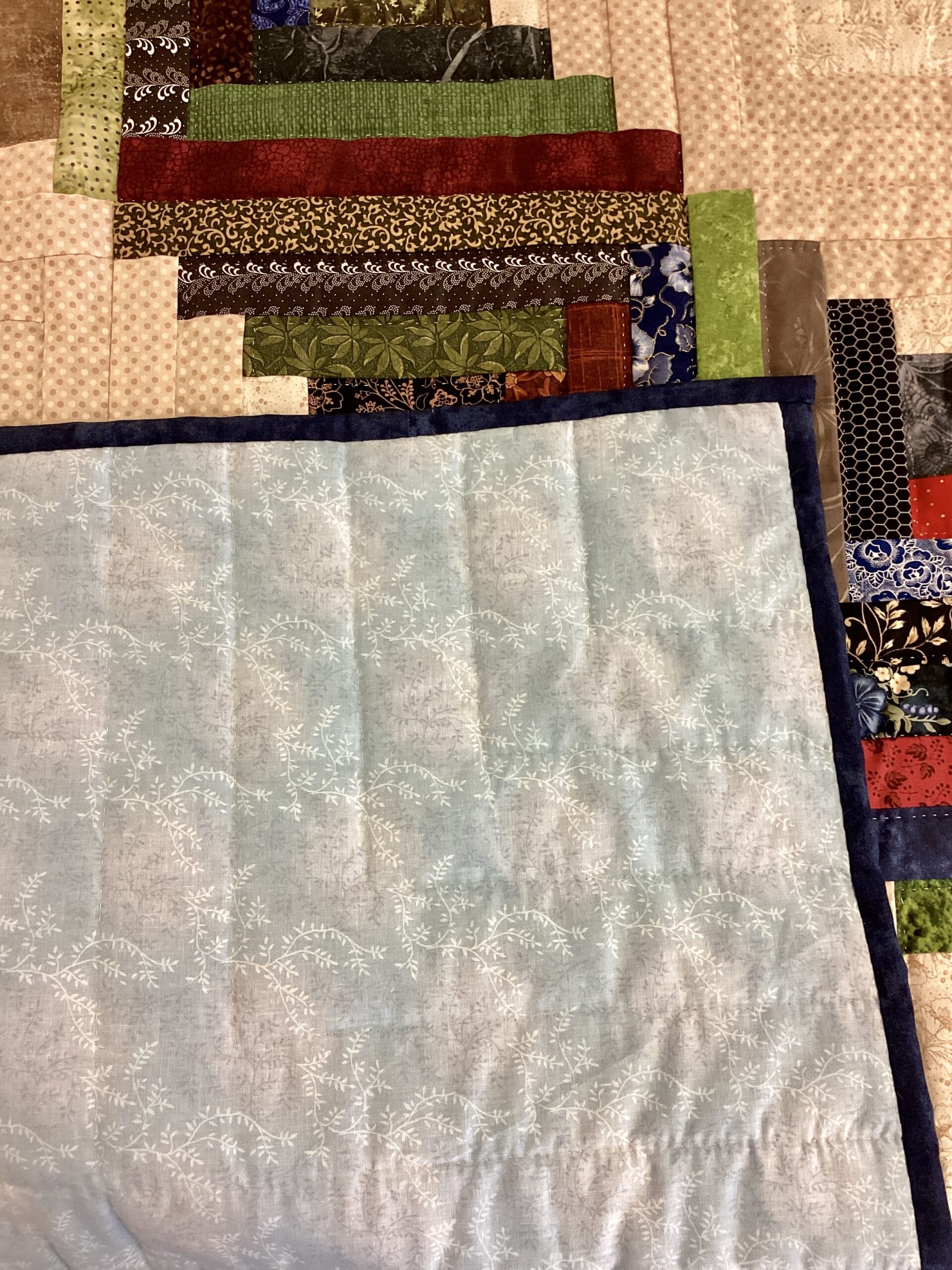 Traditional Log Cabin diamond pattern created with assorted colorful patchwork fabrics on cream backgroaLatte floral vine backing fabric on handmade Amish Log Cabin quilt from Lancaster Countyund