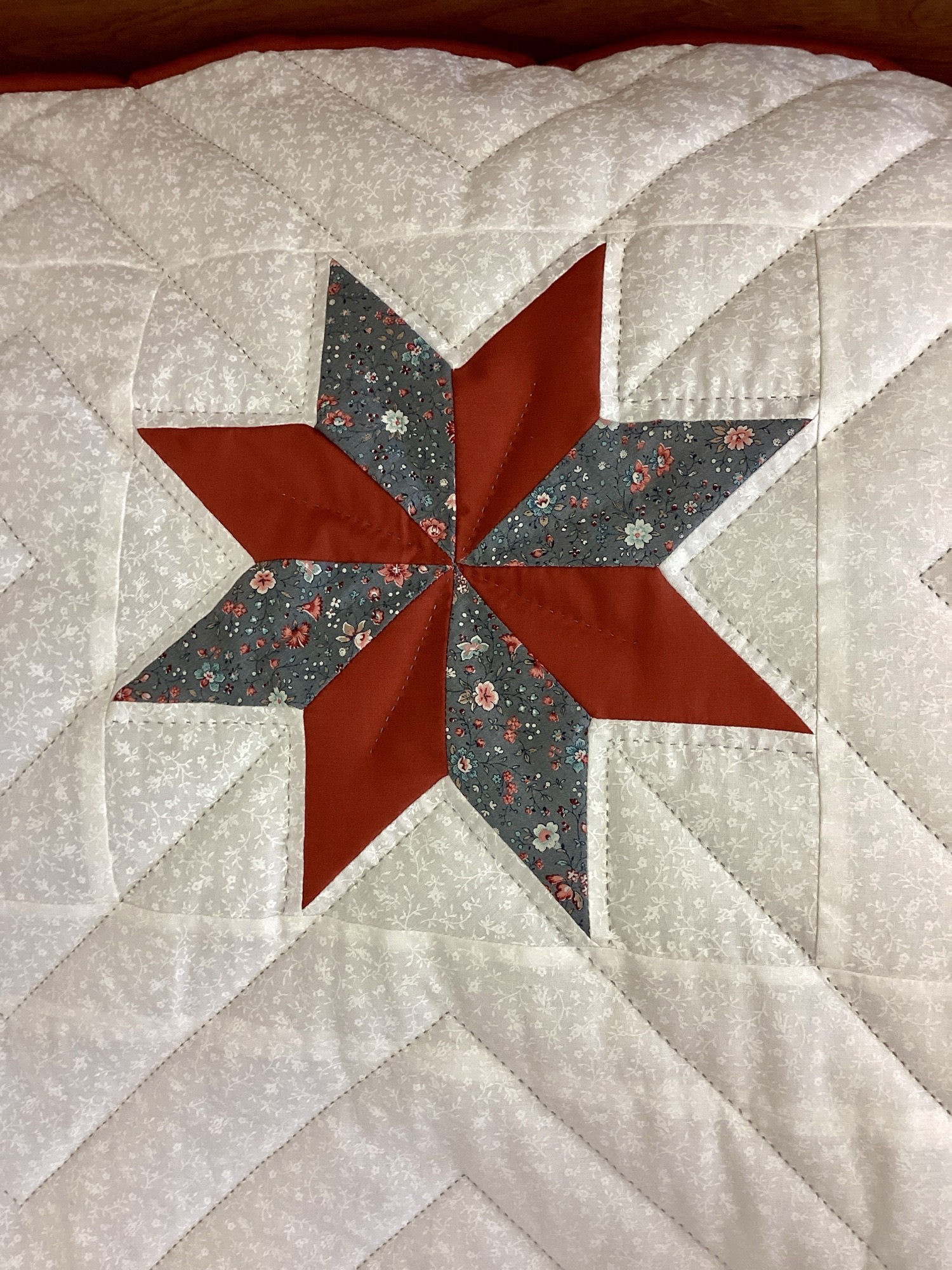 Close up of star on Handmade Lancaster County Amish Maryland Star quilt with red, white and gray center star, octagon border, feather quilting and scalloped edges