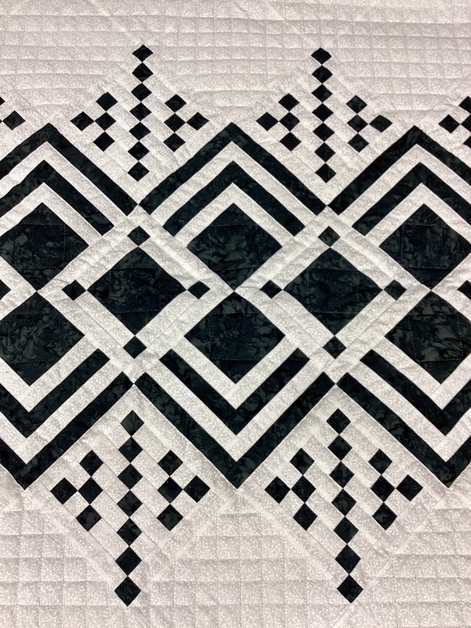 Close-up of geometric diamond piecing in black and cream tonal fabrics on handmade Queen of Diamonds quilt