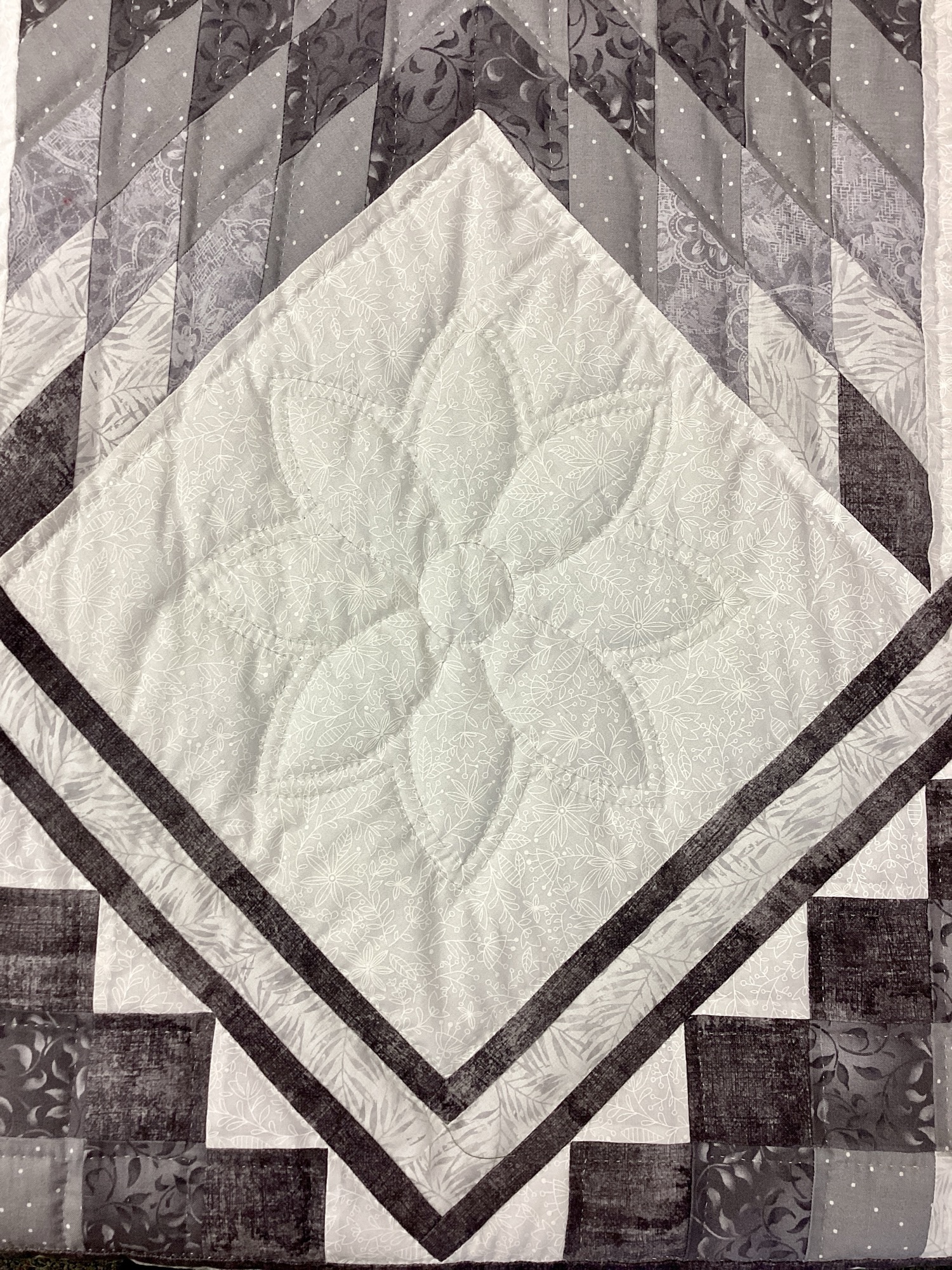 Close-up of floral hand quilting motif in white setting block of gray Star N Common quilt