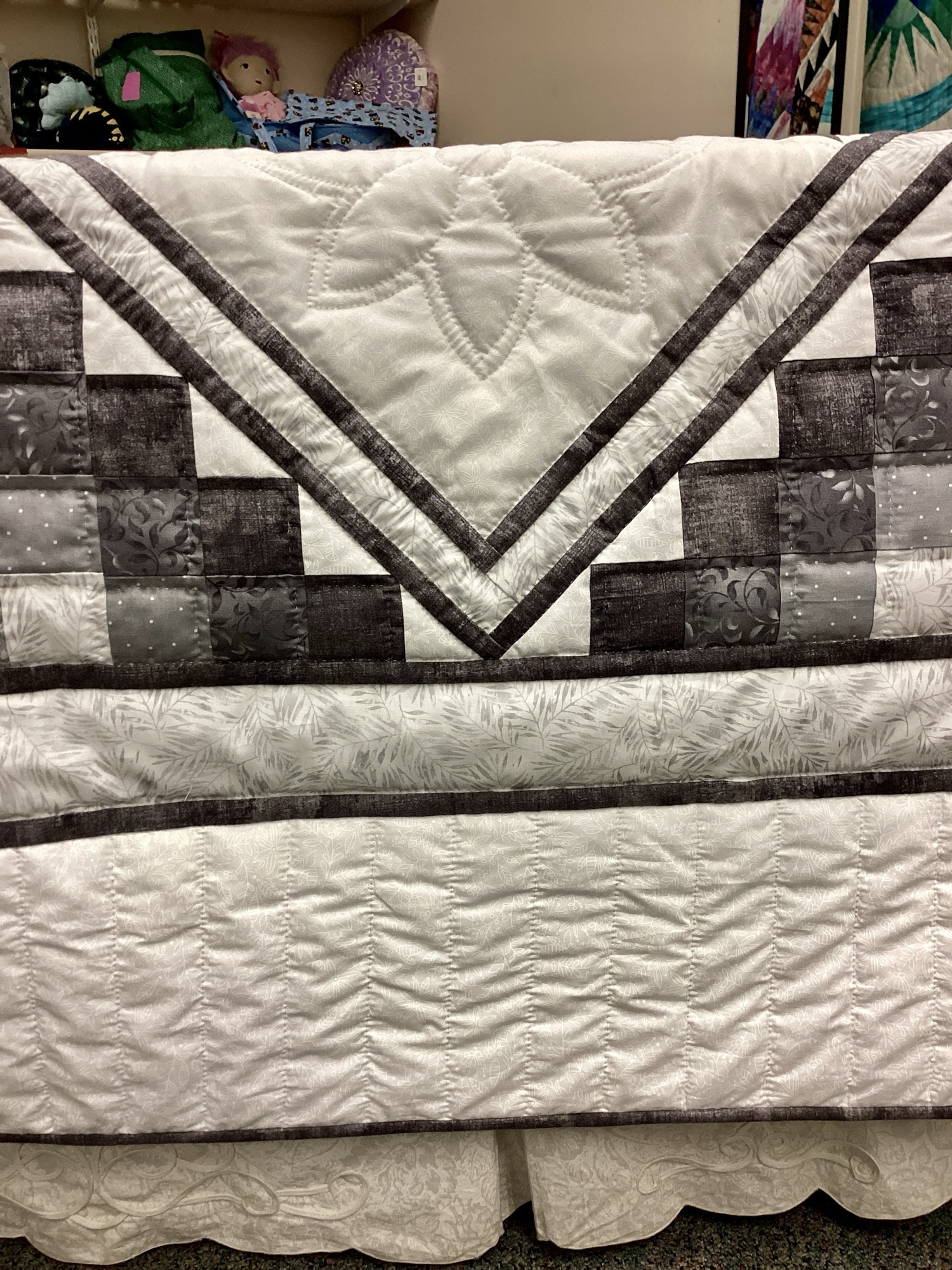 Close-up of straight edge with dark gray binding and hand quilted scroll design on gray and silver Star N Common quilt