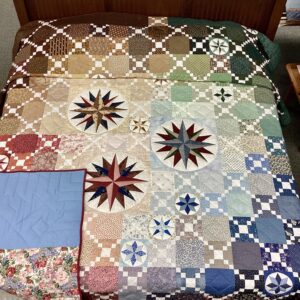 Handmade Lancaster County Mennonite Susquehanna Compass quilt with rainbow patchwork and Mariner's Compass medallions displayed on a king bed