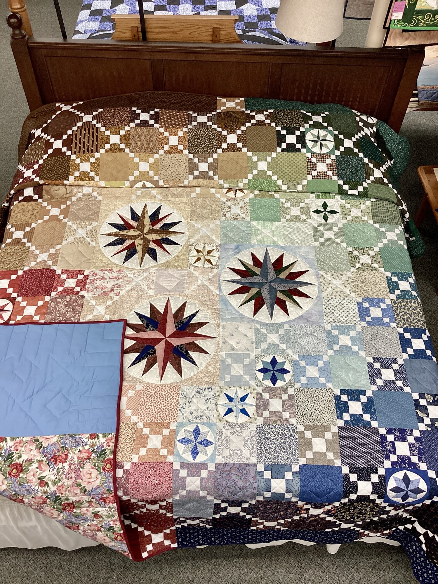 Handmade Lancaster County Mennonite Susquehanna Compass quilt with rainbow patchwork and Mariner's Compass medallions displayed on a king bed