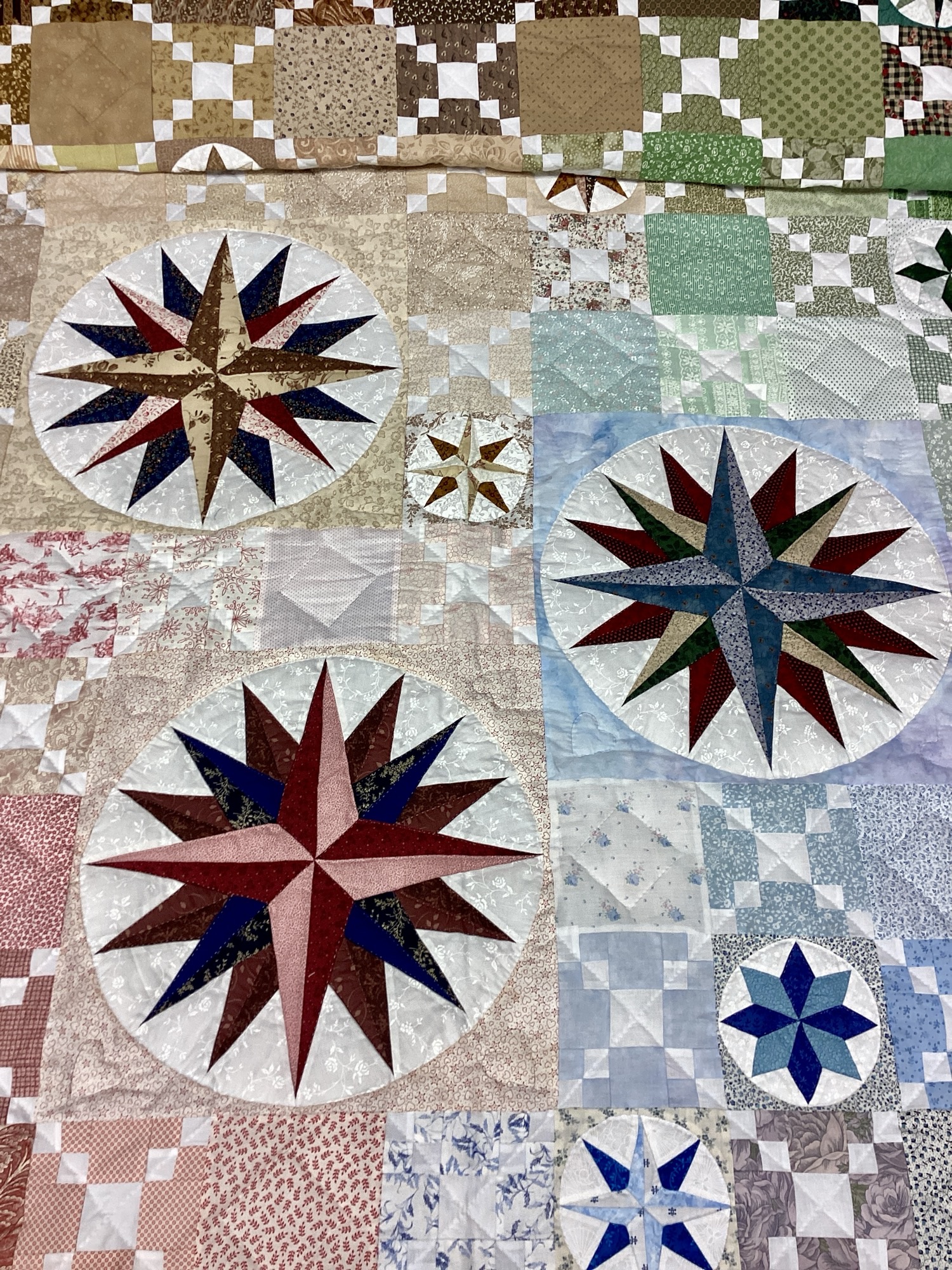 Close-up of Mariner's Compass blocks in red, blue, green and brown fabrics within the Susquehanna Compass quilt